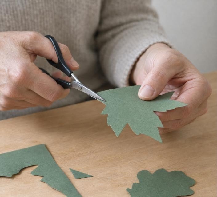 Manos recortando con tijeras una silueta de hoja en cartulina verde sobre una mesa de madera