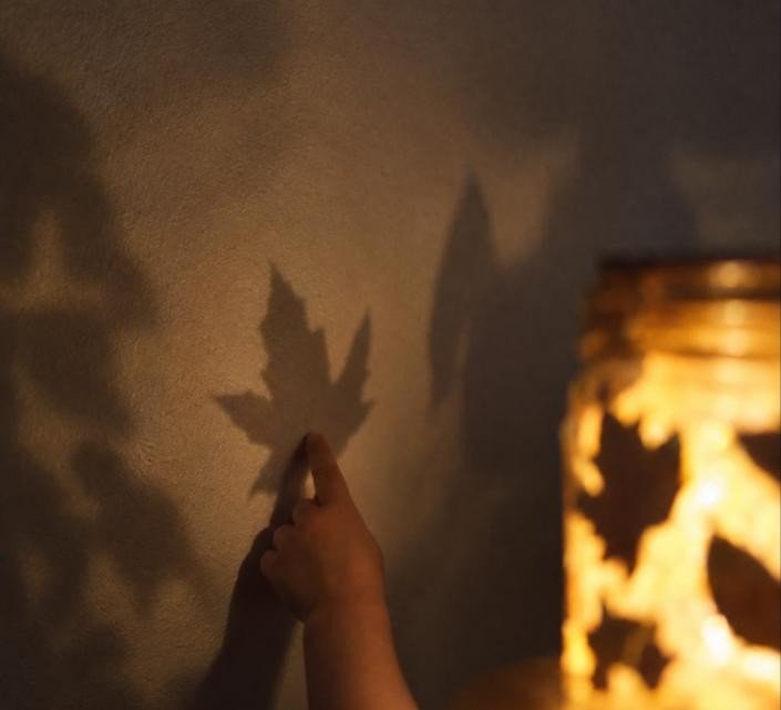 Sombras de hojas proyectadas en la pared por el bote girasombras, con una mano infantil siguiendo el movimiento