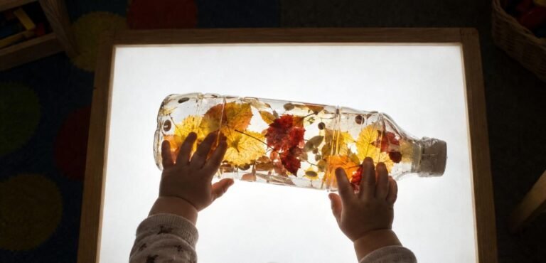 Bebé de 12 meses empujando con las dos manos una botella sensorial con hojas de otoño sobre la mesa de luz — botella sensorial de otoño
