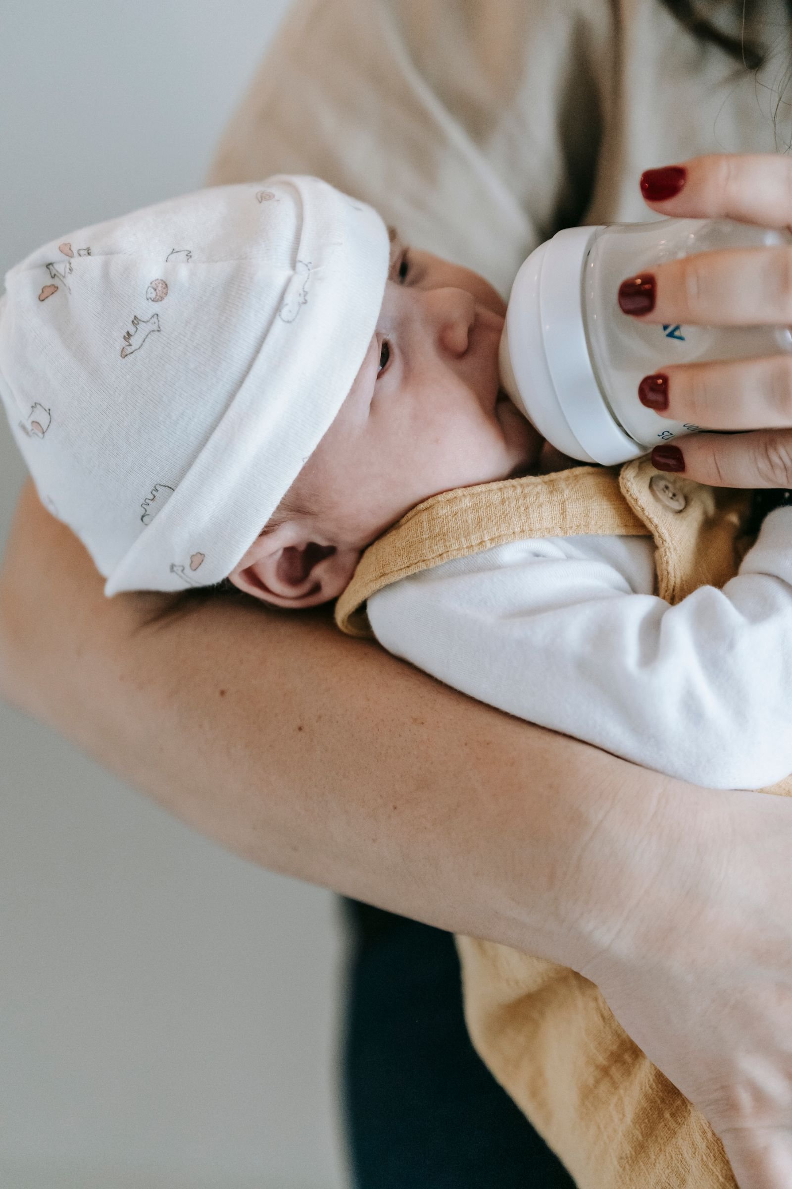 Bebé recién nacido con gorrito tomando el biberón en brazos de su madre