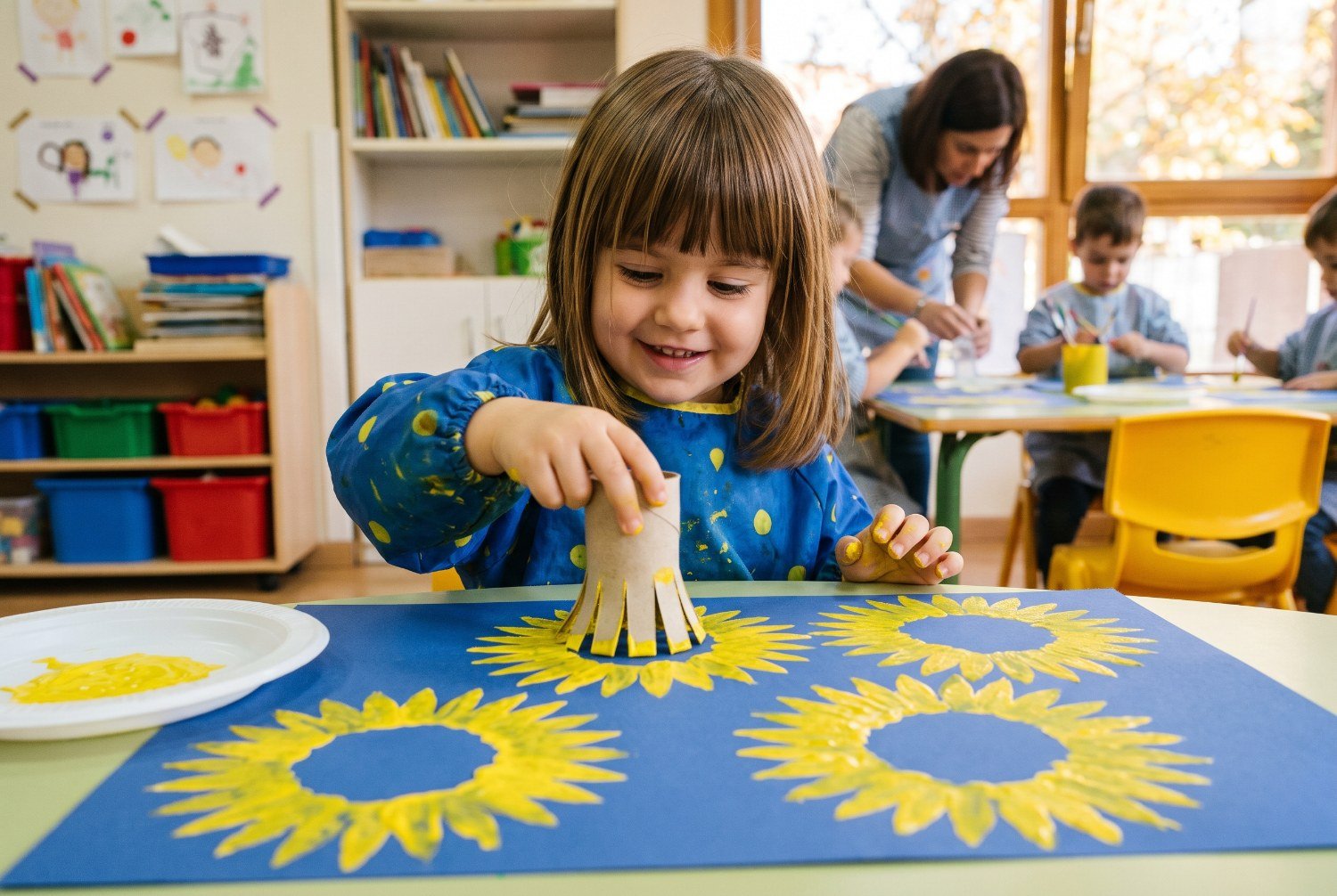 Niña de 2 años estampando girasoles amarillos con un rollo de cartón sobre cartulina azul