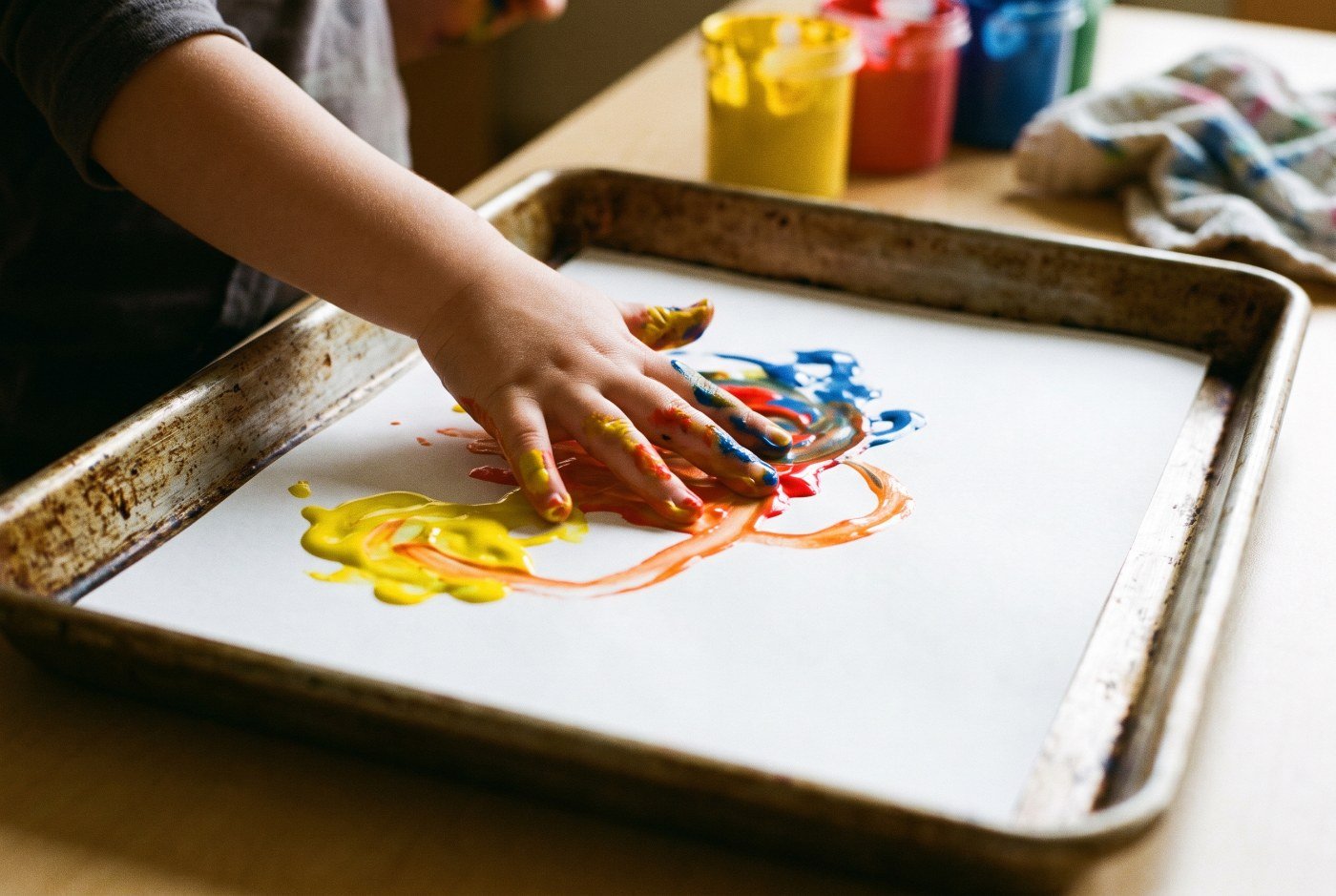 Manos de un niño extendiendo pintura de dedos amarilla y roja sobre una cartulina grande