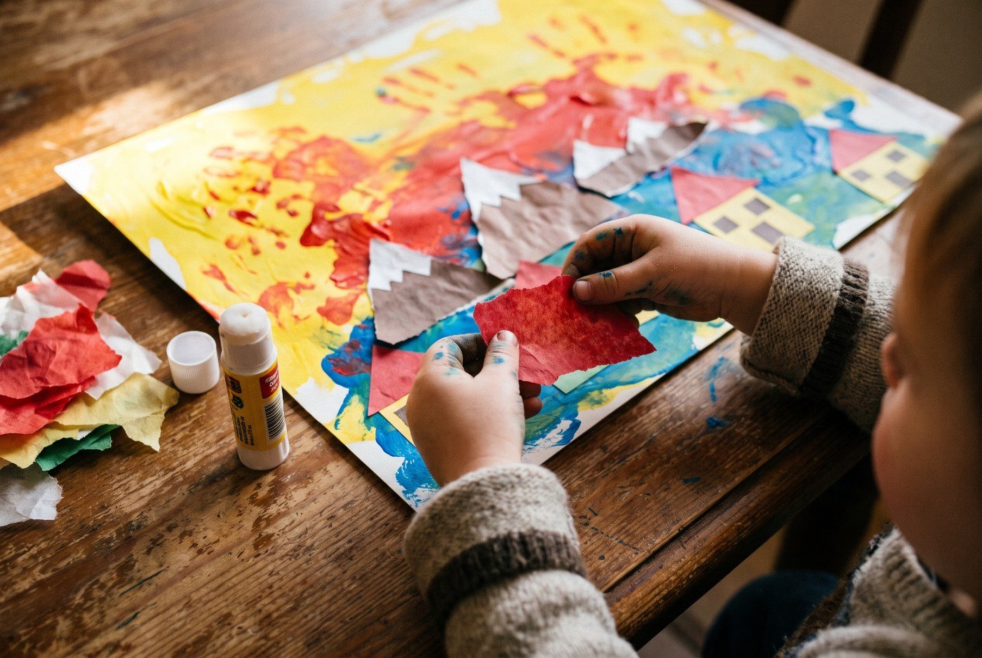 Niño de 3 años pegando trozos de papel de colores sobre su paisaje pintado con los dedos — Otoño en Murnau para niños