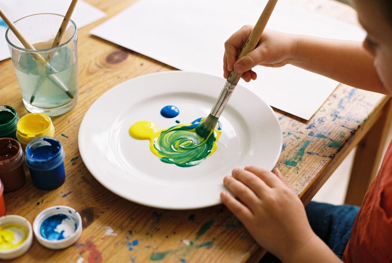 Niño de 5 años mezclando con un pincel témpera amarilla y azul en un plato blanco