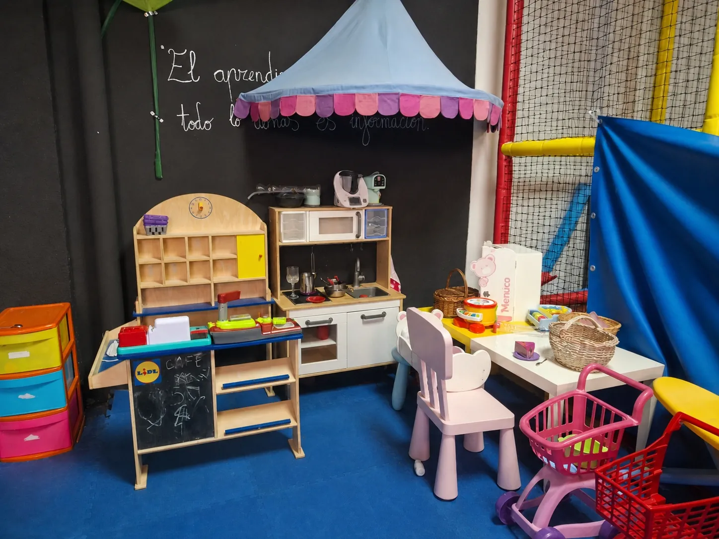 Rincón de juego simbólico con cocinita, tienda y carritos de la compra en la guardería