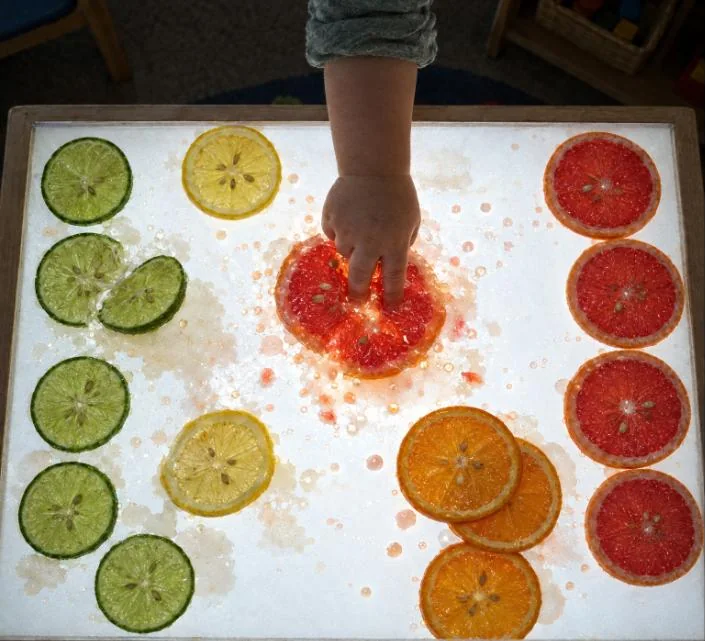 Dedos de un niño apretando una rodaja de pomelo y soltando zumo sobre el cristal